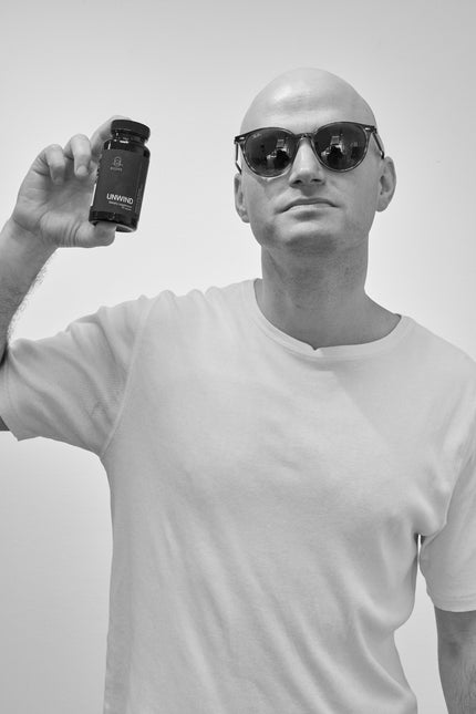 Man wearing sunglasses and holding a bottle of Unwind against a plain background