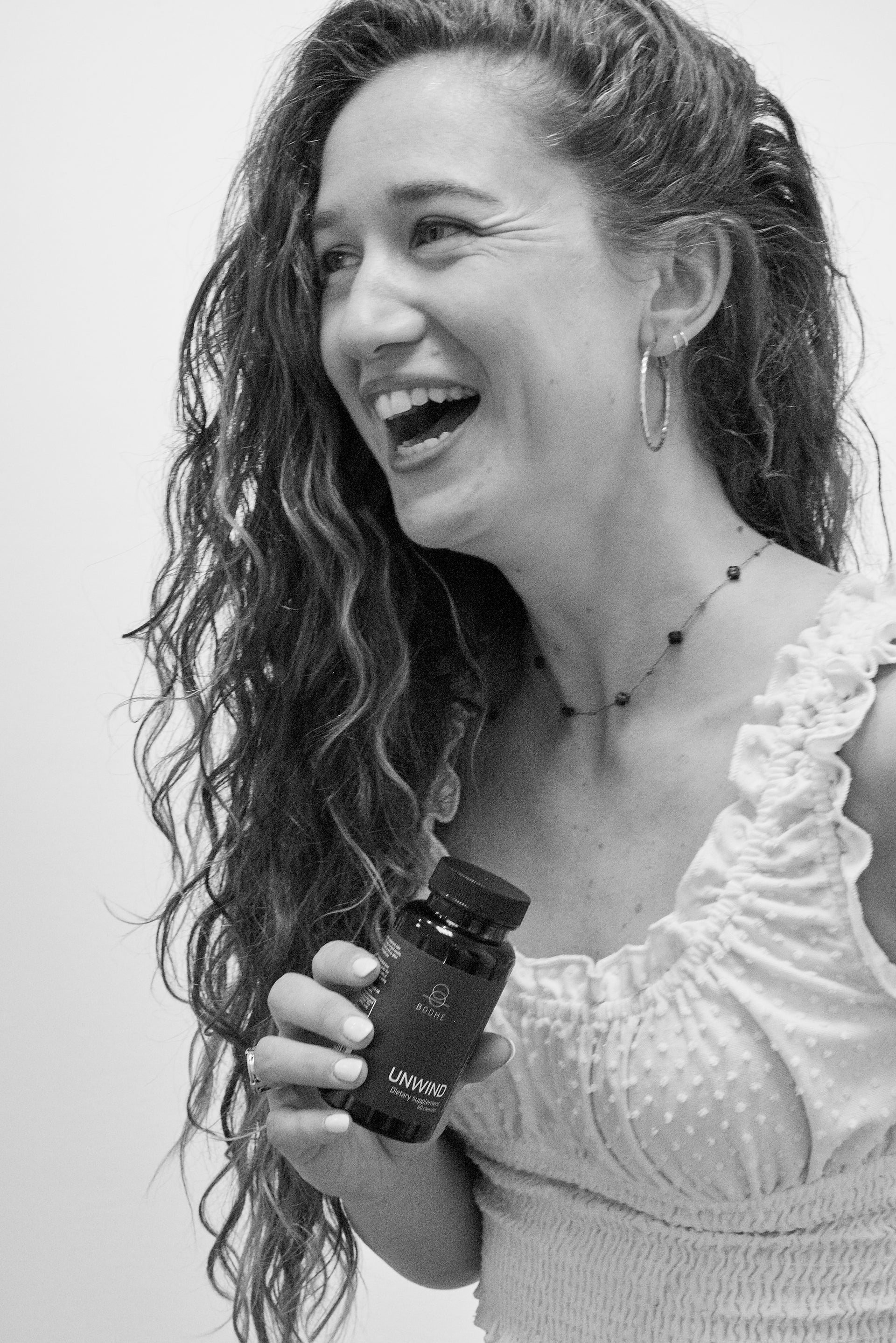 A black and white photo of a girl holding a bottle of stress management supplements and laughing