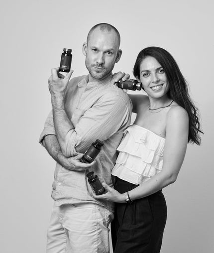 Black and white photo of a man and woman holding bottles against a plain background