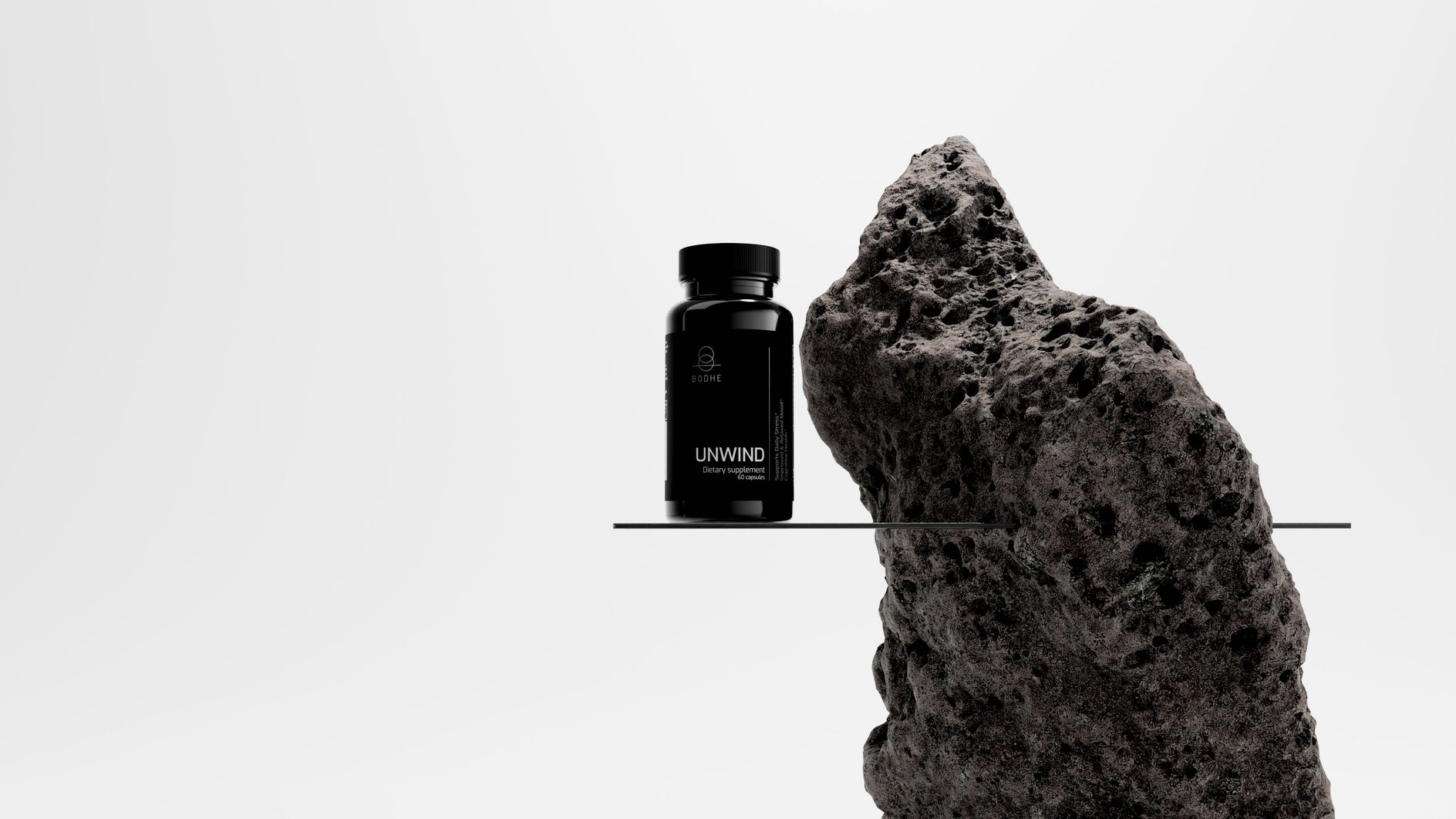 Black bottle labeled 'UNWIND' next to a textured stone on a white background